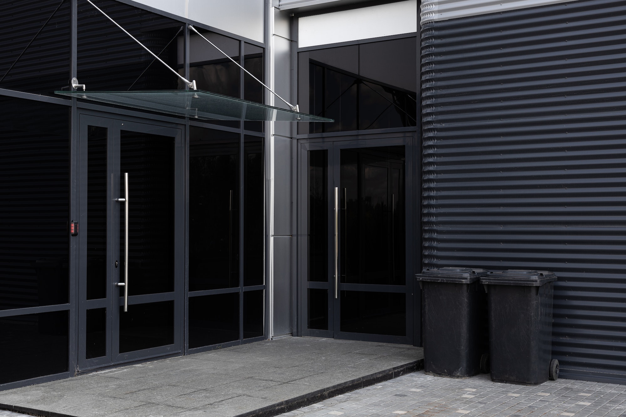 Black glass doors - entrance to modern building and two scratched black dustbins against black metal